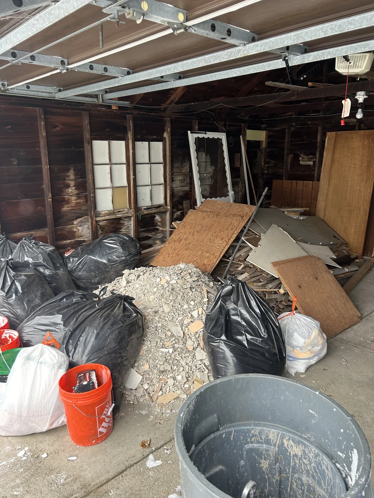Garage bay packed with contractor bags, plaster rubble, plywood and scrap lumber before removal